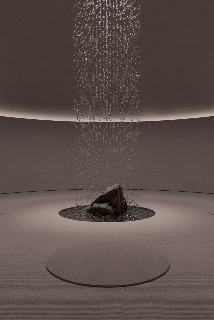 A tranquil interior space featuring a central stone surrounded by water droplets cascading from the ceiling, creating a serene atmosphere.