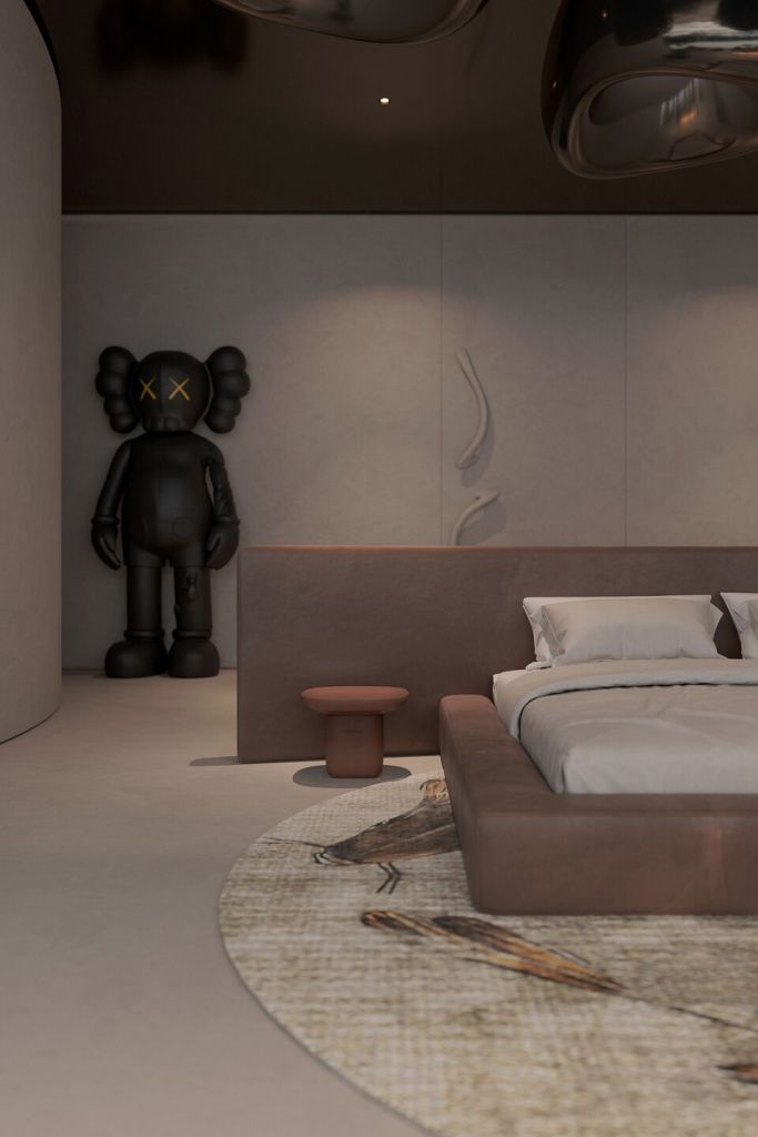 A modern bedroom interior featuring a low bed with neutral bedding, a small round table, and a Kaws figurine in the corner, complemented by a circular rug with a nature motif.