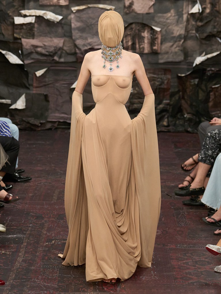 model posing in a beige transparent dress as she descends down the runway