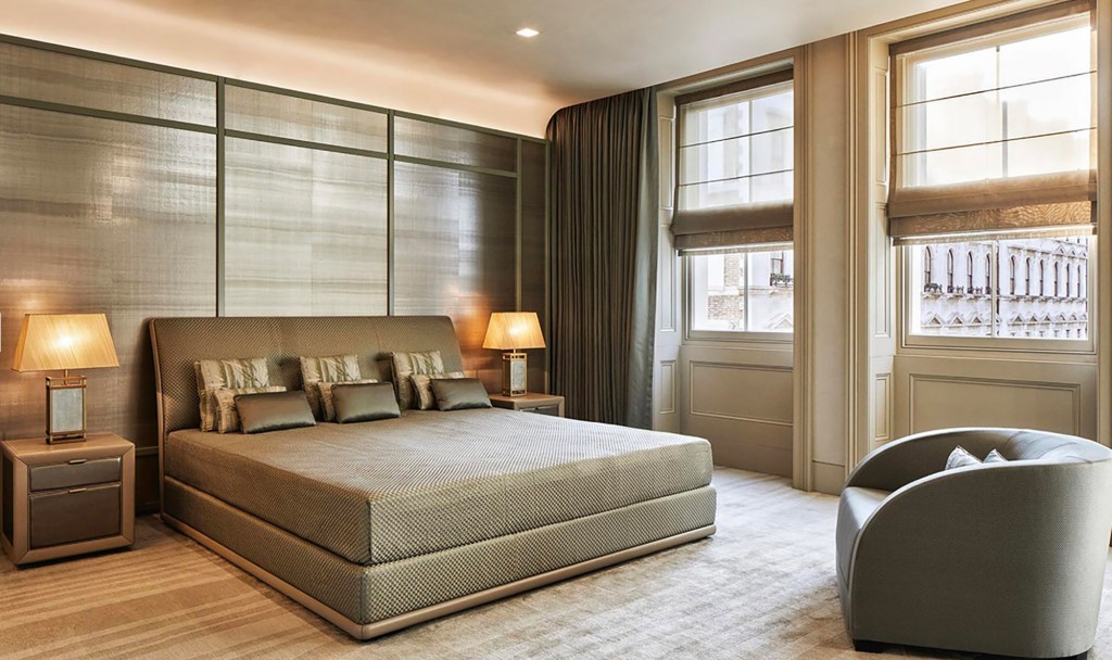 Elegantly designed bedroom featuring the kind size bed with multiple cusions and open windows. Colour palette is subtle in beige with gold accents.