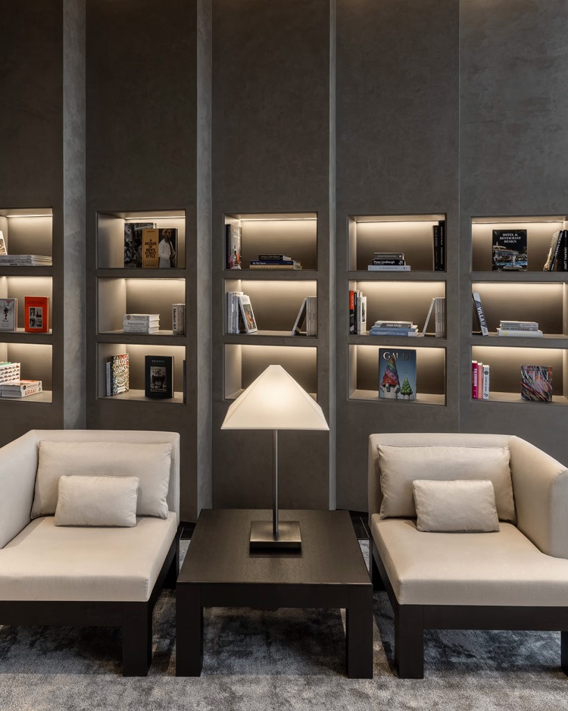 Chic and sober library space with bookshelves, long lounges and wooden table with a reading lamp.