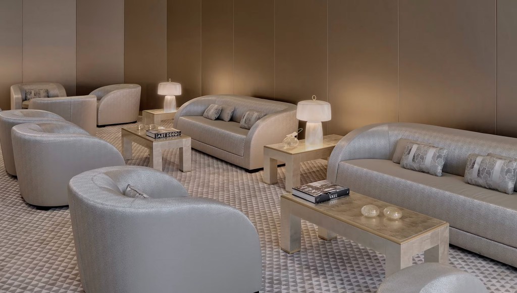 Hotel lobby with multiple two-seater couches, chairs and low tables, all in subtle grey and beige tones.