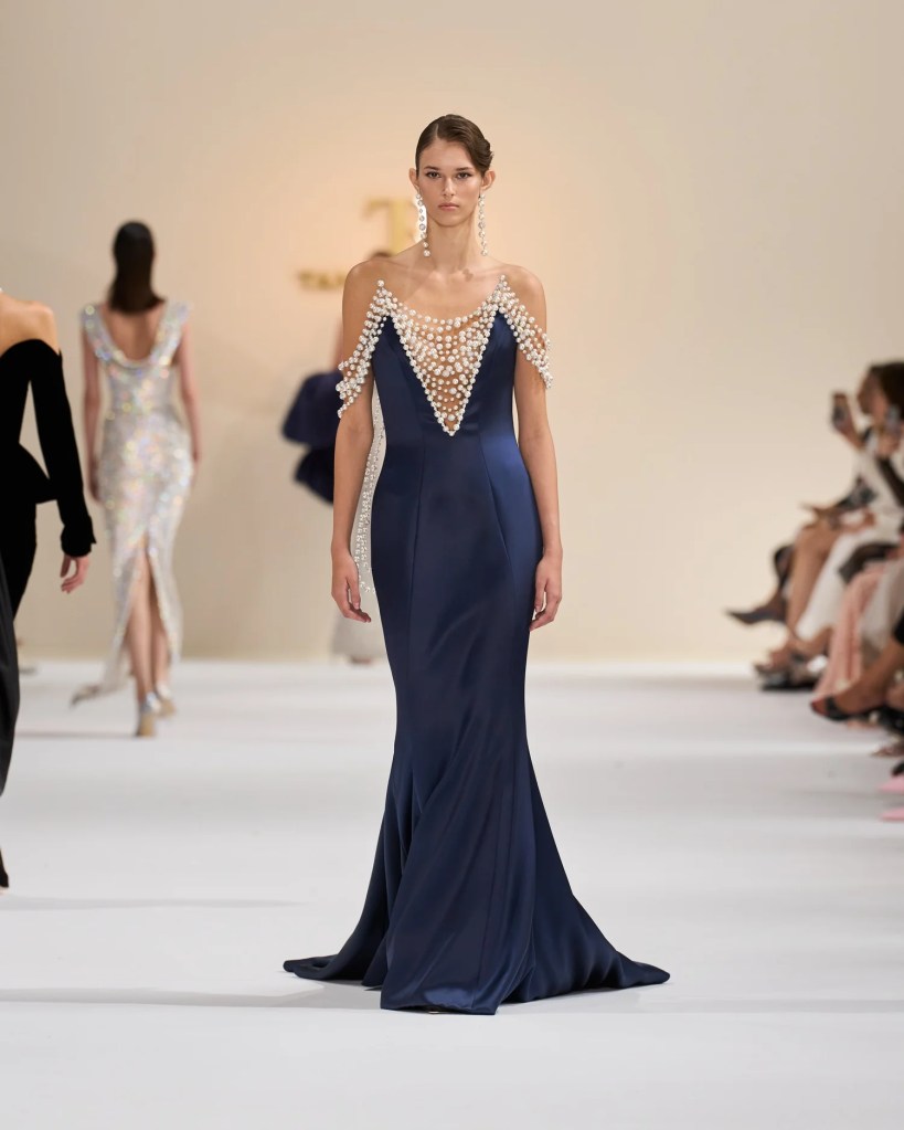 A model walks down the runway in a navy gown with pearl embellishments.