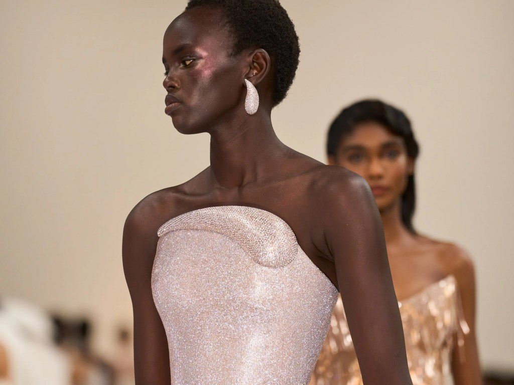 Model showcasing a sparkling light pink gown with a strapless design, featuring intricate detailing, set against a soft neutral background.