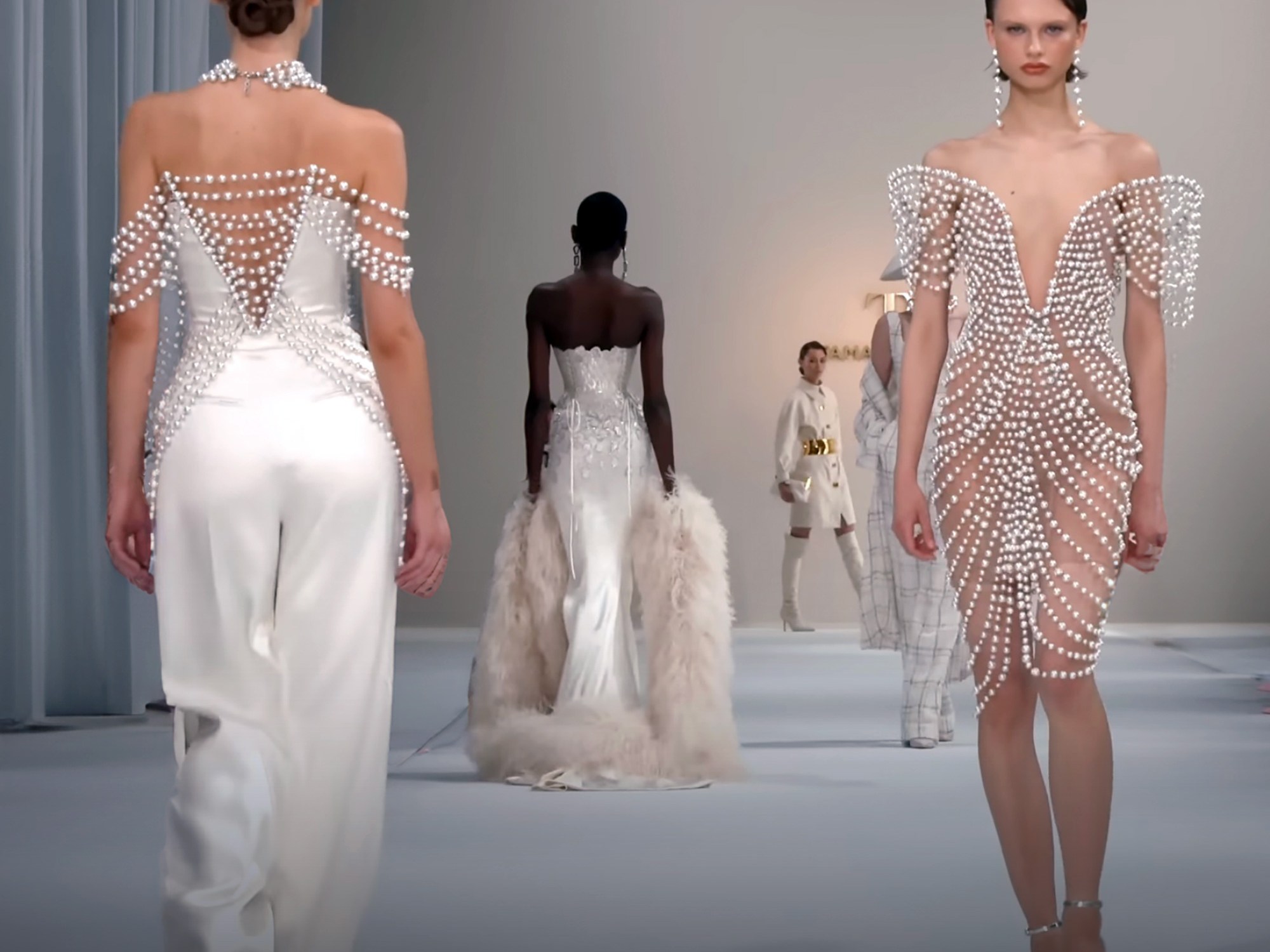 Catwalk models walking the runway in white outfits with pearl accessories in Paris.