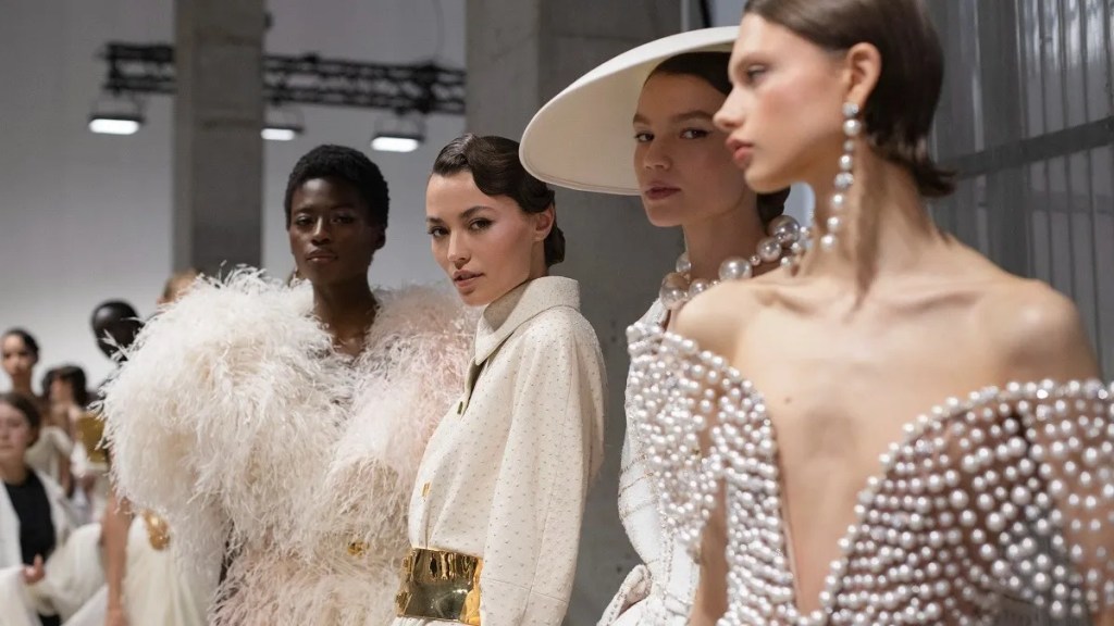 Haute couture runway models posing in white and cream evening gowns.