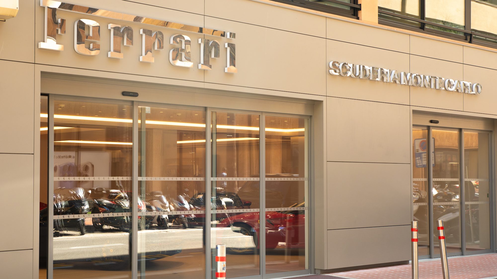 Glass-fronted Ferrari dealership exterior, with reflective signage. Inside, luxury cars are visible. The setting feels sleek and sophisticated.
