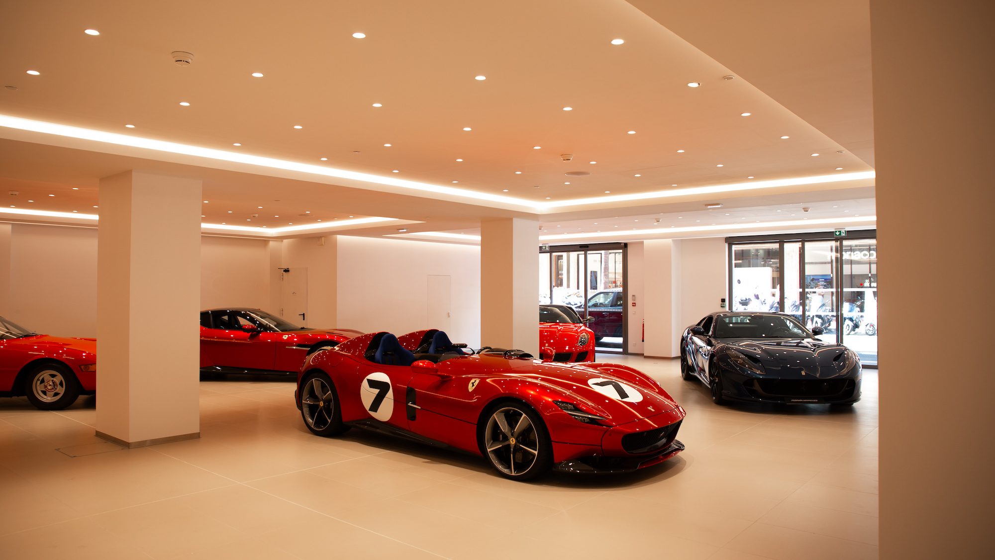Luxury car showroom with sleek, red and black sports cars, each with unique designs. Bright, modern lighting highlights their glossy finishes.