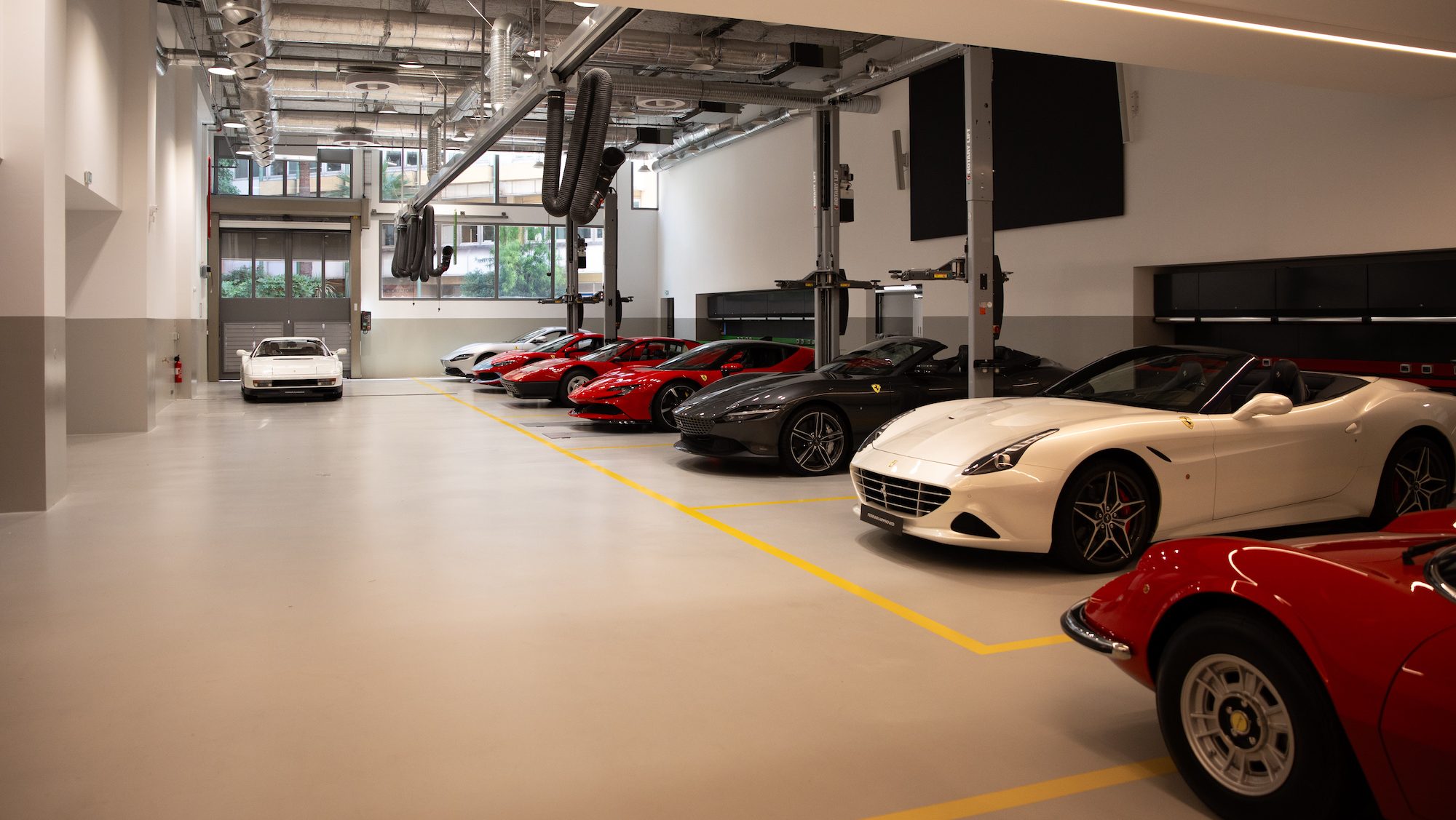 Modern garage with sleek sports cars, including red and white models, parked under bright industrial lighting. The space conveys luxury and precision.