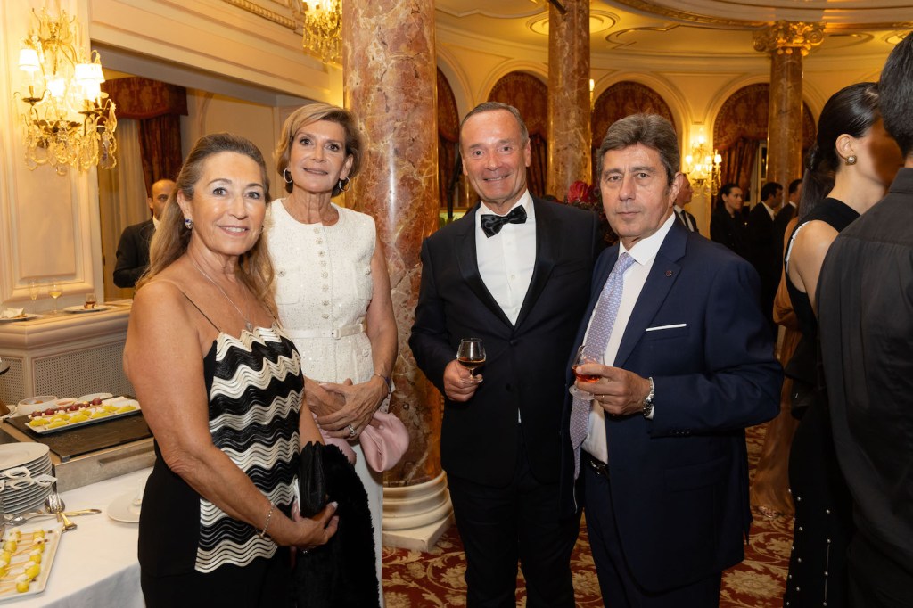 A group of elegantly dressed people smiling together at an event in the ornate Salle Belle Époque, with a table of appetizers visible in the background.