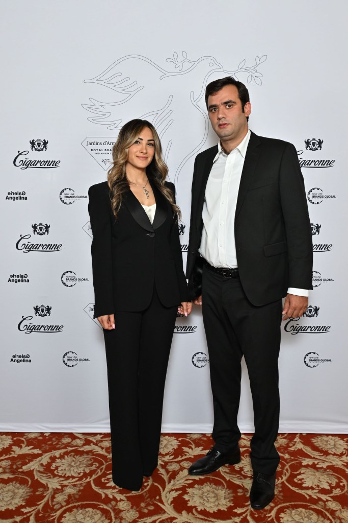 A man and a woman dressed in formal attire pose together in front of a branded backdrop featuring the logo of Jardins d'Arménie and Cigaronne.