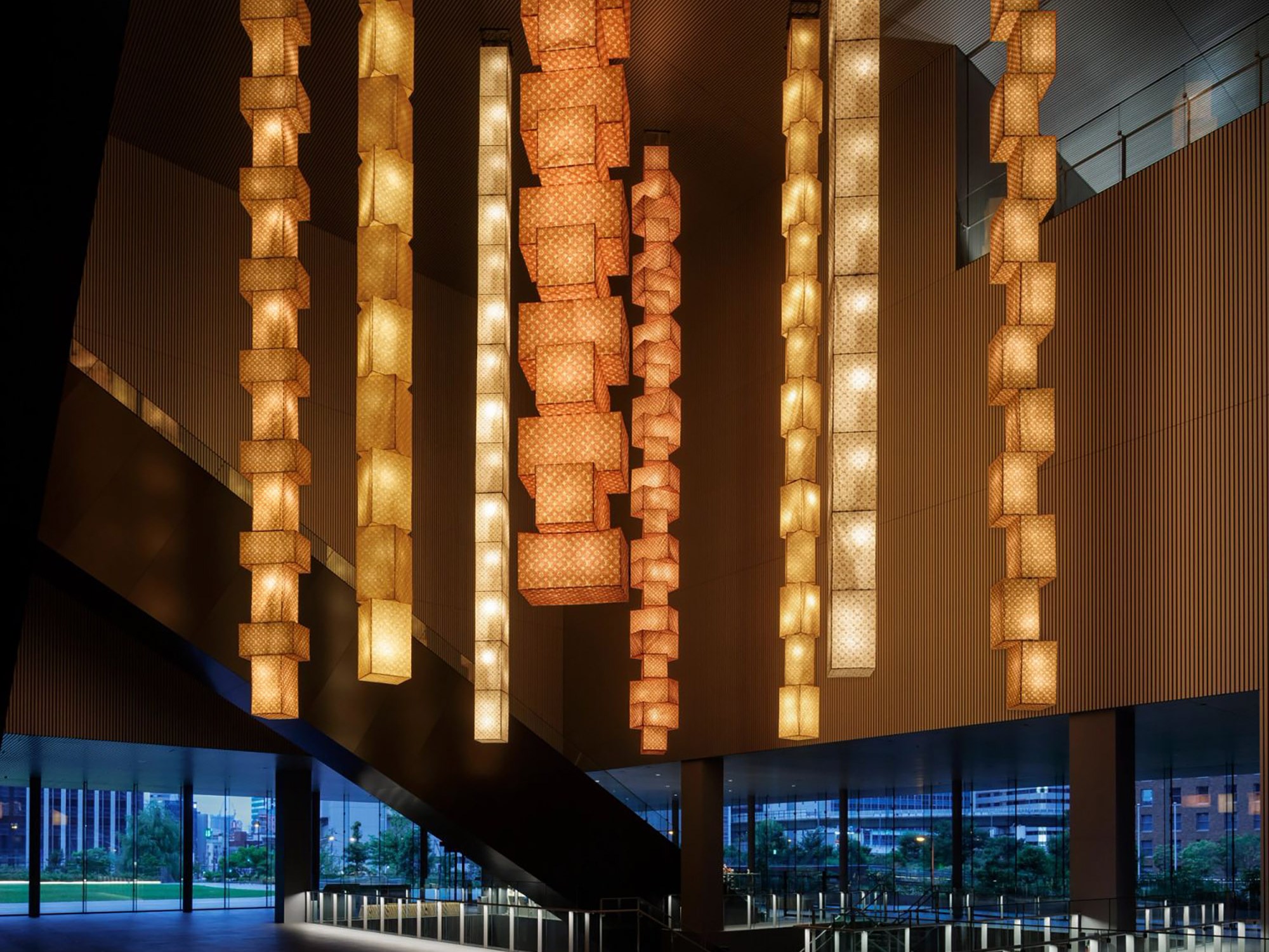 Illuminated pendant lights hang in a modern lobby, casting warm glows against sleek walls and large windows revealing the evening skyline.