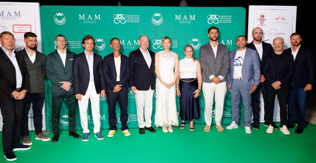 Group photo featuring Princess Charlene and Prince Albert II alongside various attendees at the 2025 Monaco Cup, all dressed elegantly against a branded backdrop.