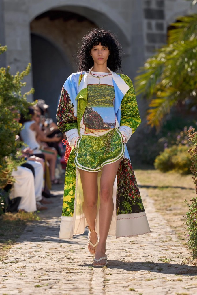 Alémais model wears lightweight shirt and shorts with a long summer coat in green, blue and white colours