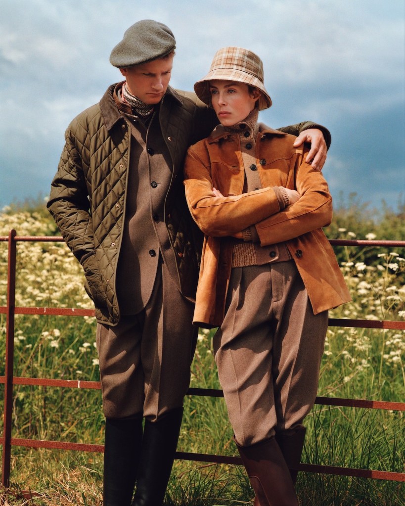 Man hugs woman, both leaning on the fence and wearing Loro Piana cvlothing in shades of brown.