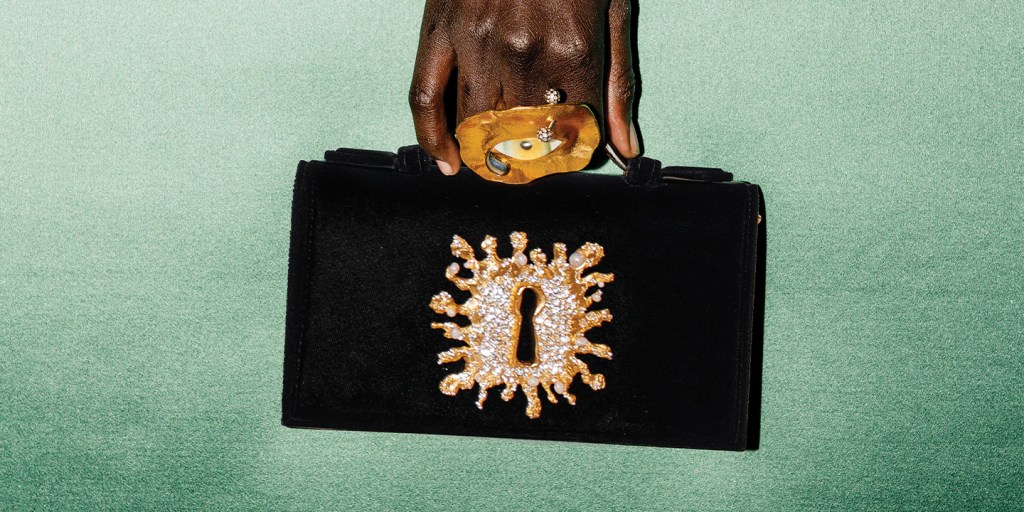 Schiaparelli black velvet handbag with gold keyhole embelilshed with diamonds, held in a dark skinned hand