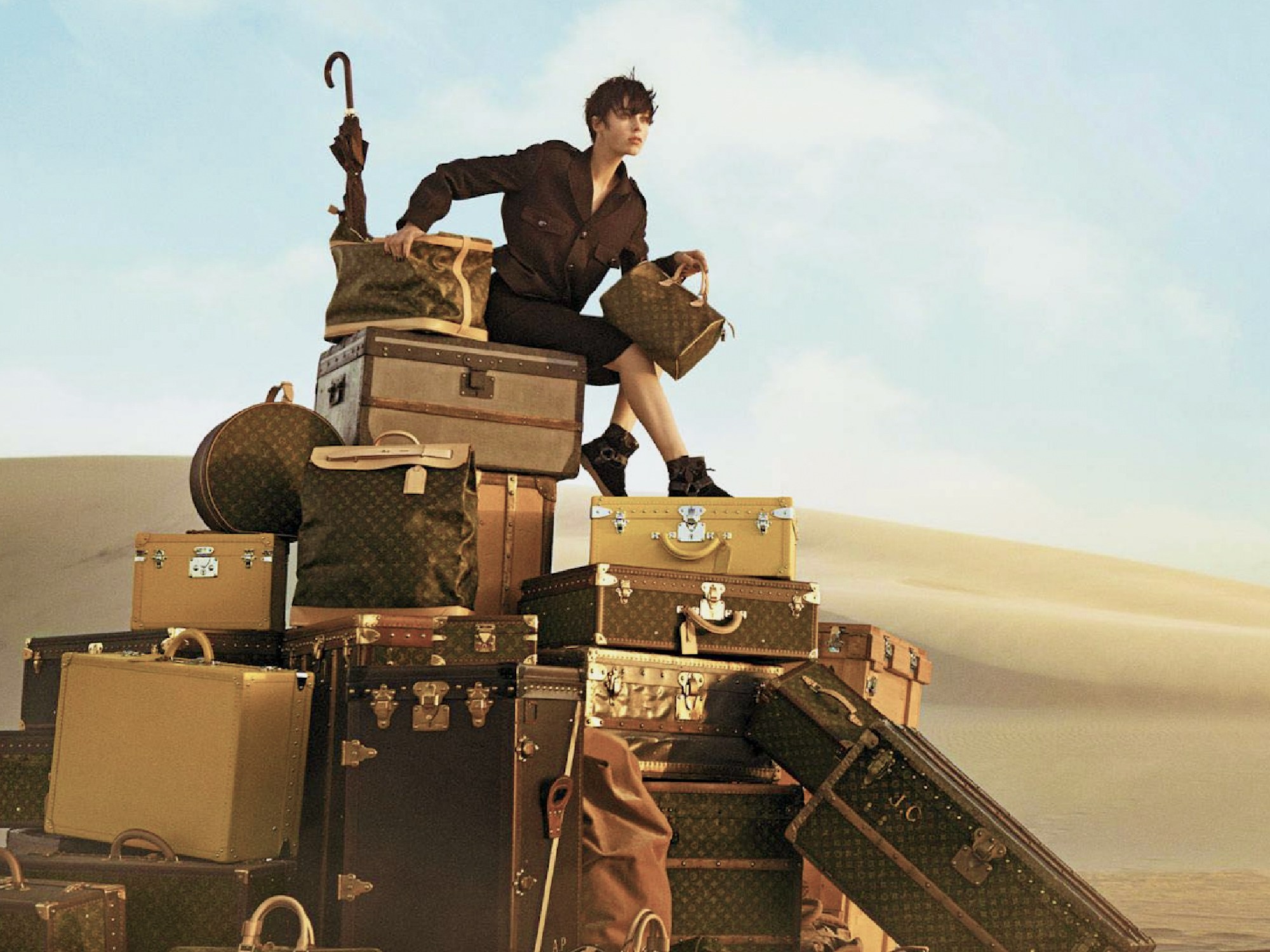 LV monogram trunks, bags and luggage suitcases with a model sitting on top of them in the desert