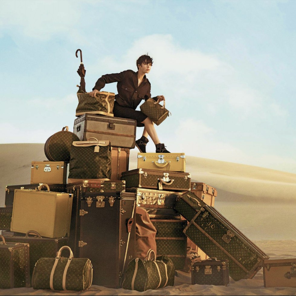 LV monogram trunks, bags and luggage suitcases with a model sitting on top of them in the desert