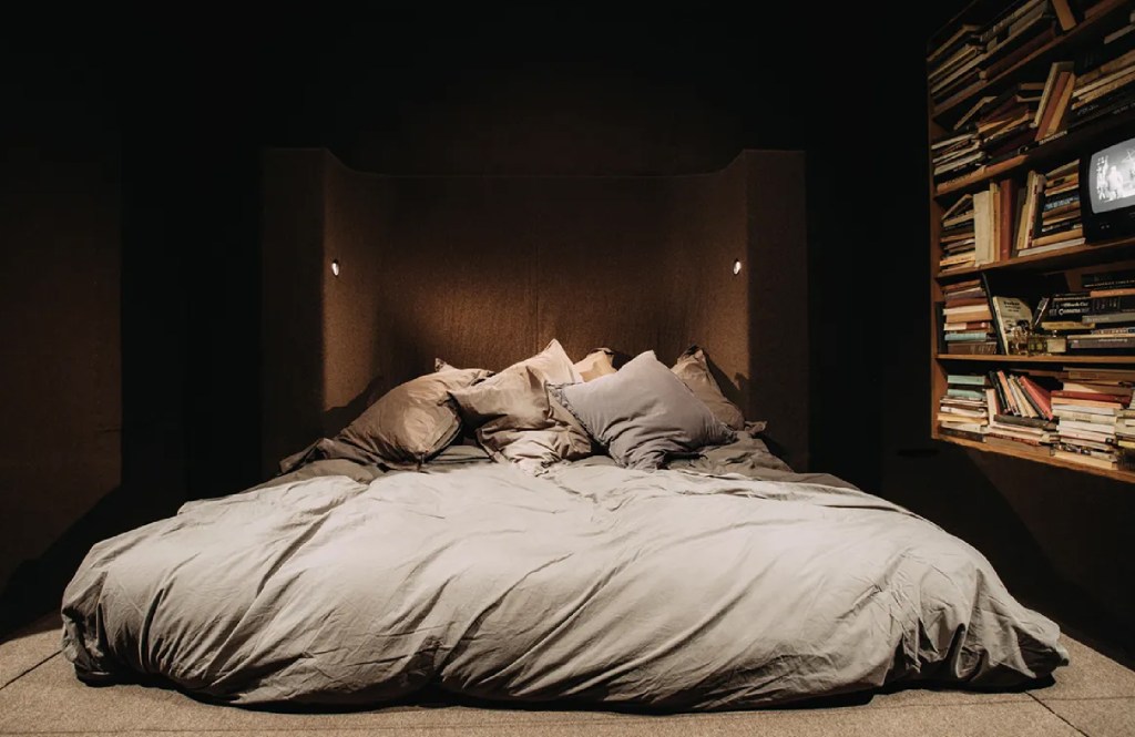 Rick Owens bedroom with creased bed sheets and messy book shelf