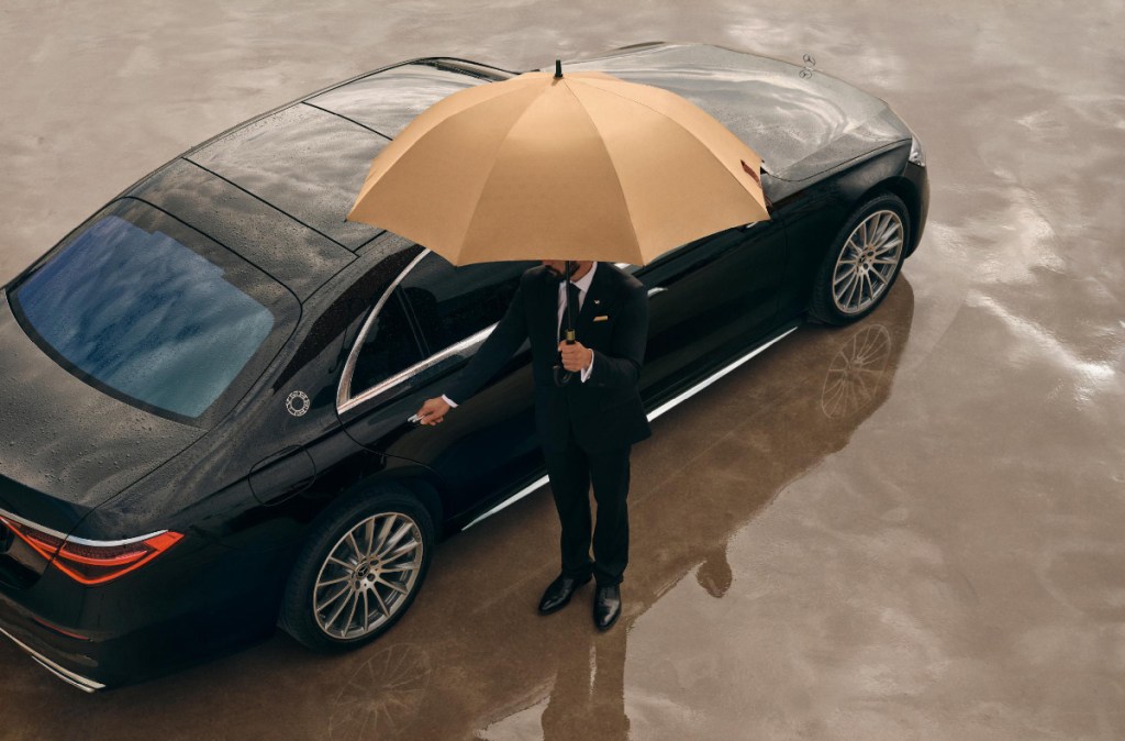 discreet private driver with an umbrella waiting for the vip client by the maybach wheely branded black car
